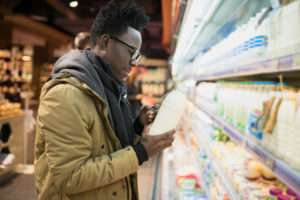 African man reading milk bottle label in supermarket 