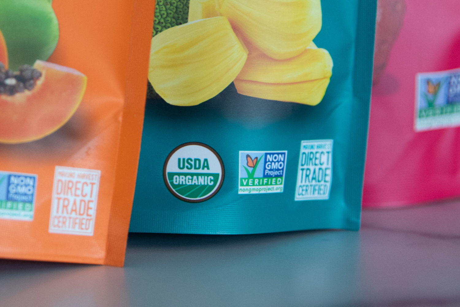 Non-GMO Project Mark and USDA Organic seal placed side by side on the bottom of a dried fruit product packaging