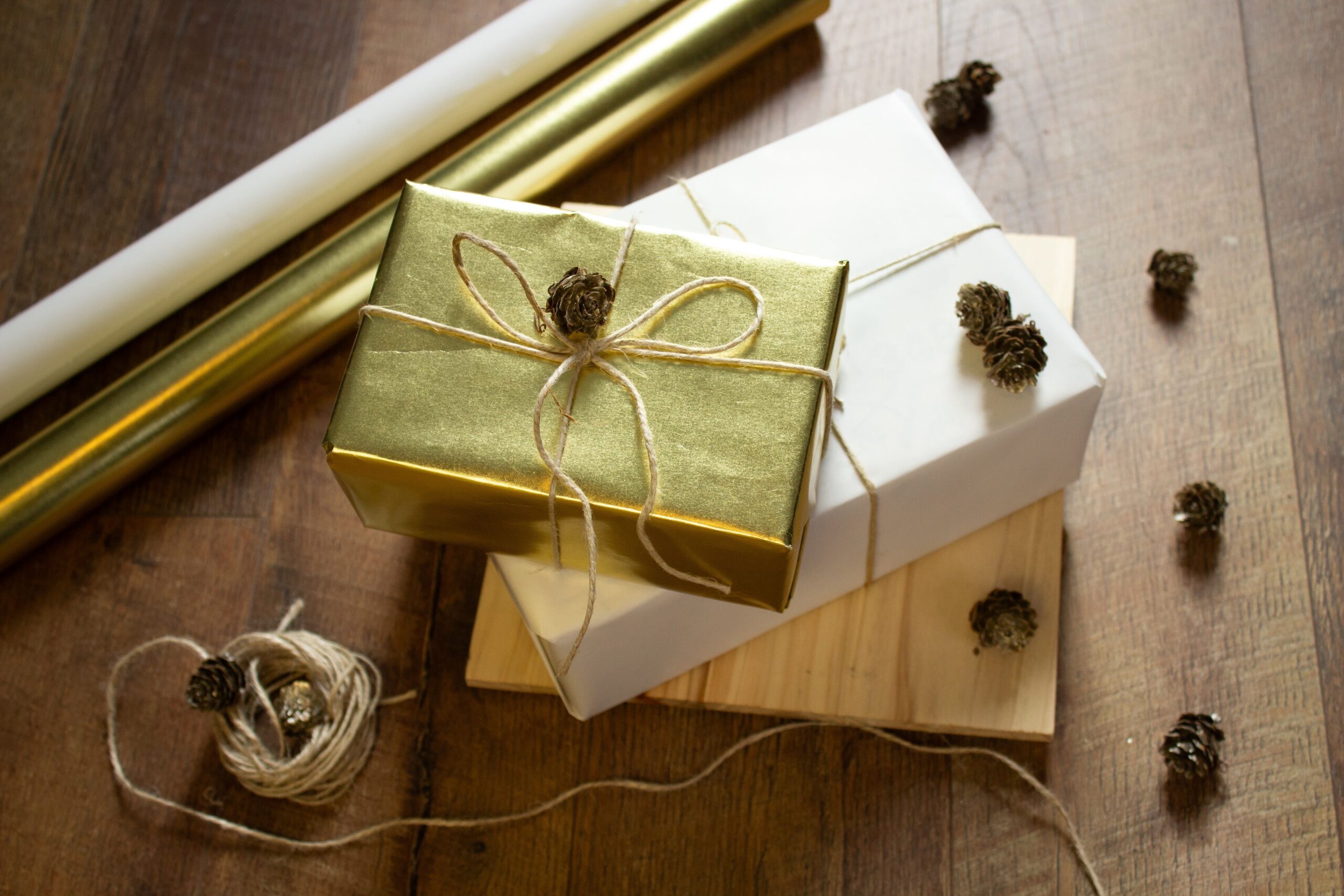 A golden foil wrapped gift box sits on top of another wrapped gift box with golden wrapping paper sitting in the background